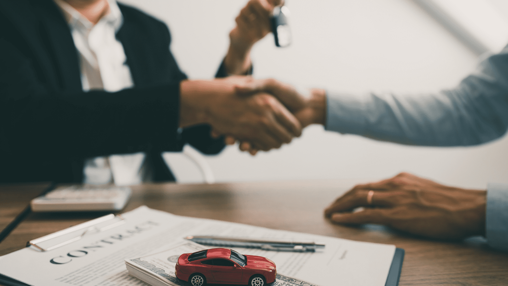 Red car on a desk with handshake in the background.
