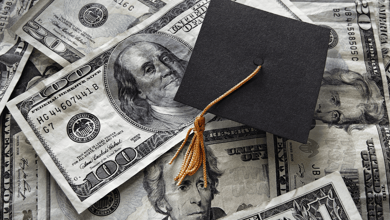Graduation cap placed on scattered $100 bills symbolizing financial achievement.