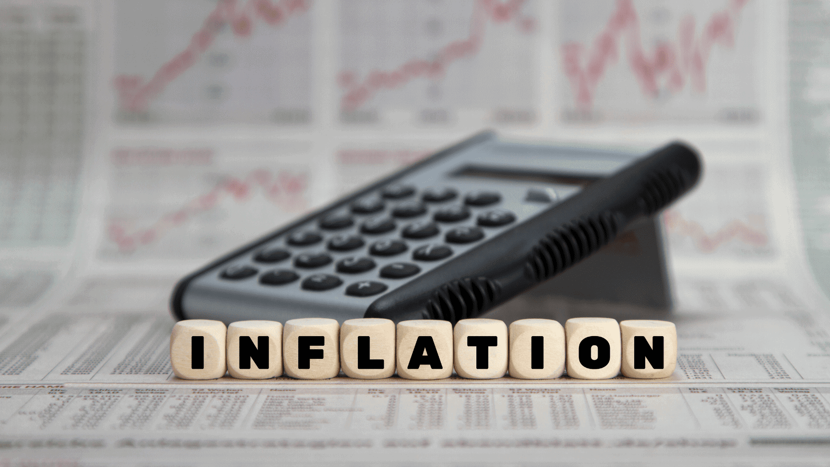 Calculator and newspaper showing financial data with wooden blocks spelling "INFLATION".