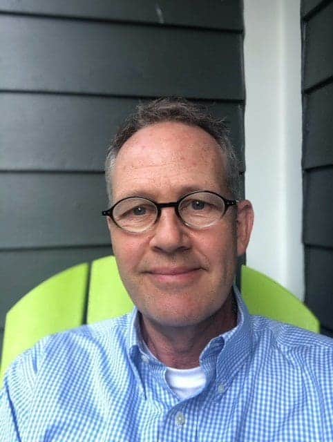 Friendly man with glasses taking a selfie outdoors.