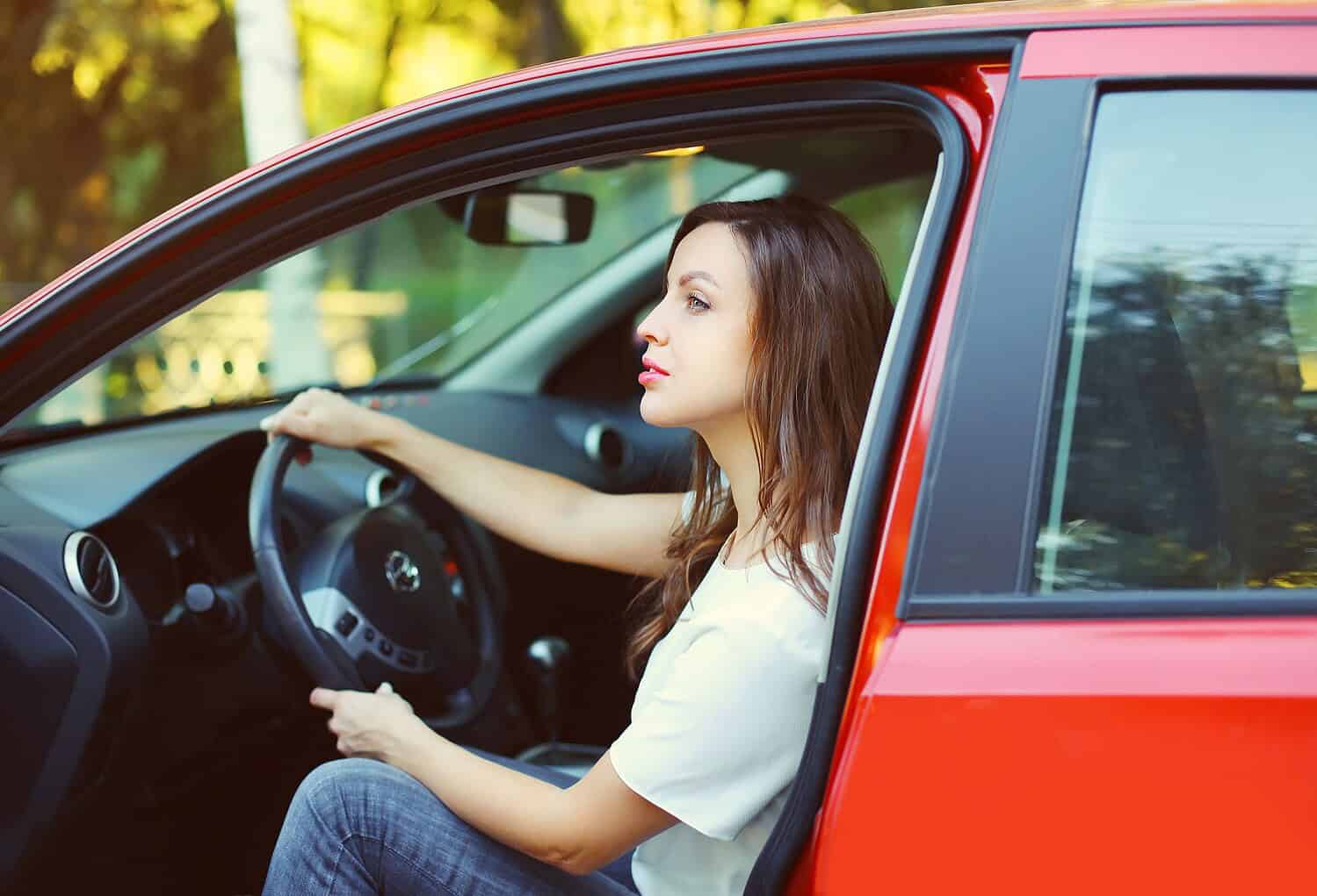 Young woman driving a red car with window open, enjoying the ride.
