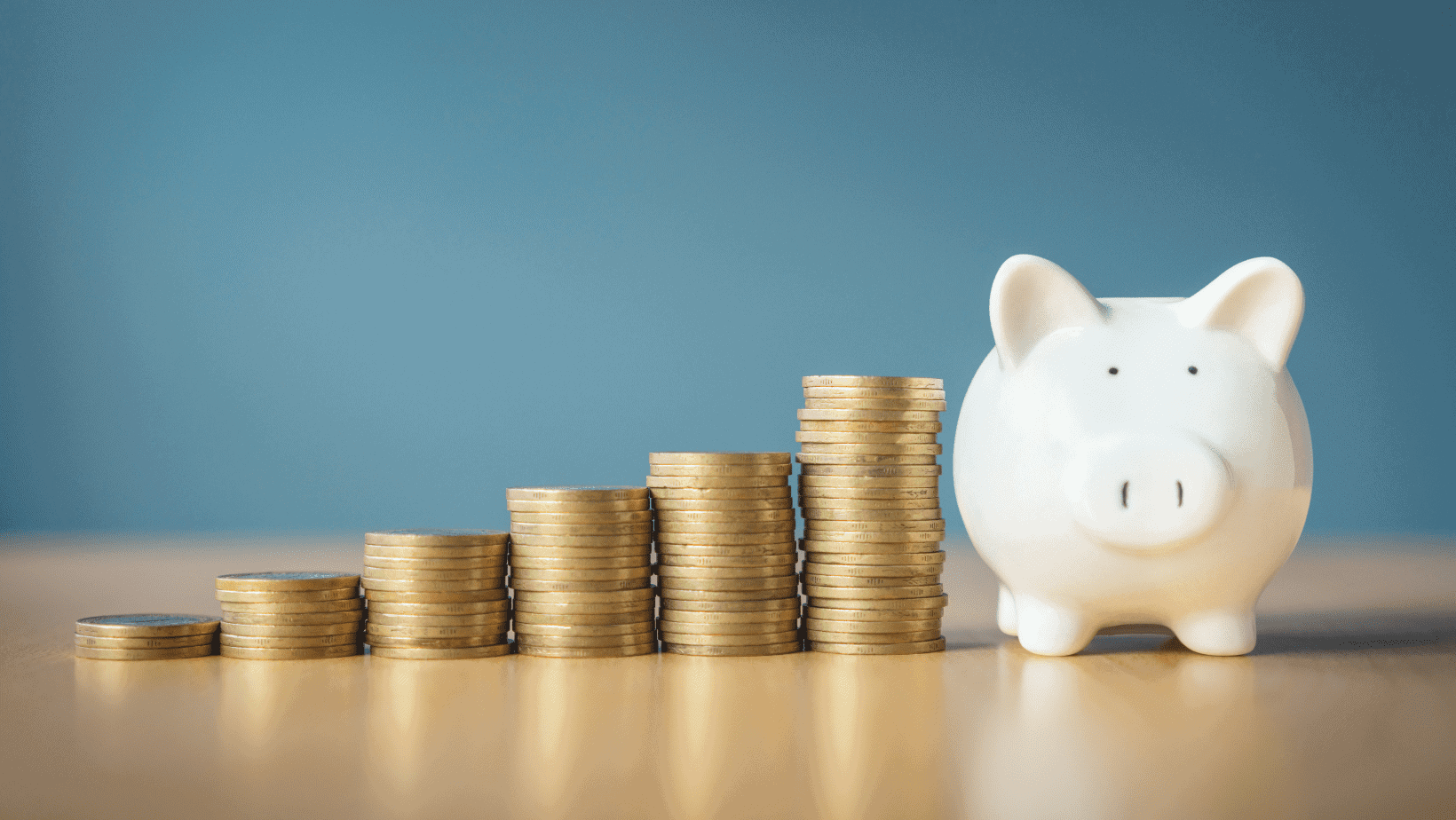 Coins increasing in size next to a white piggy bank on a blue background.