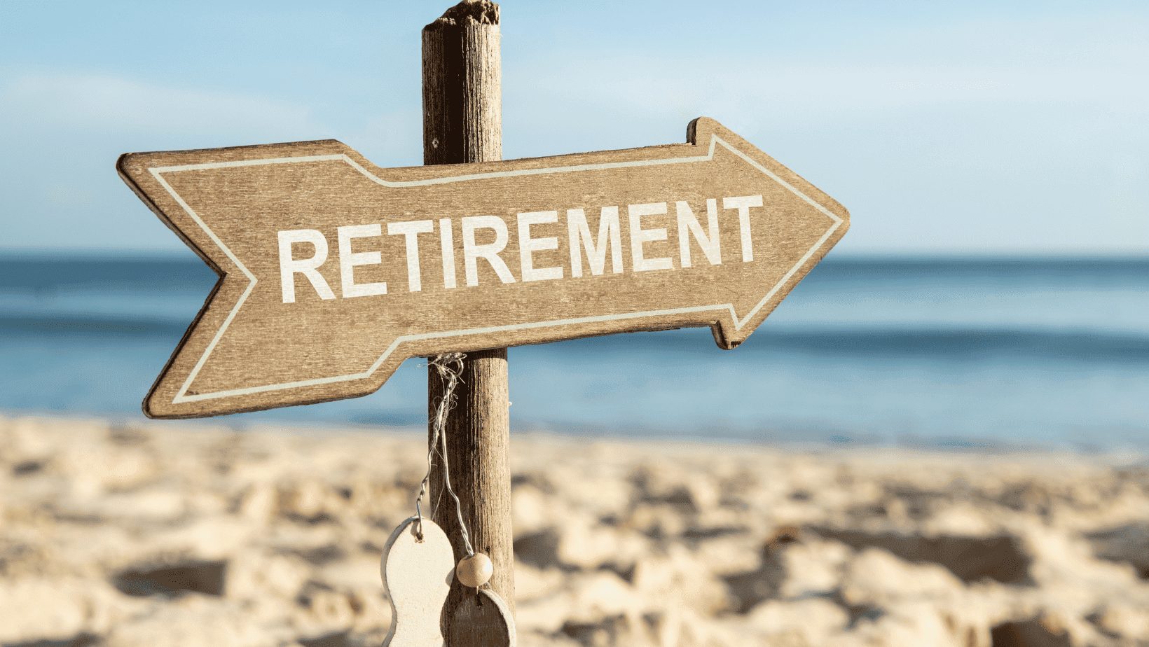Wooden sign with "RETIREMENT" text pointing right, on sandy beach.