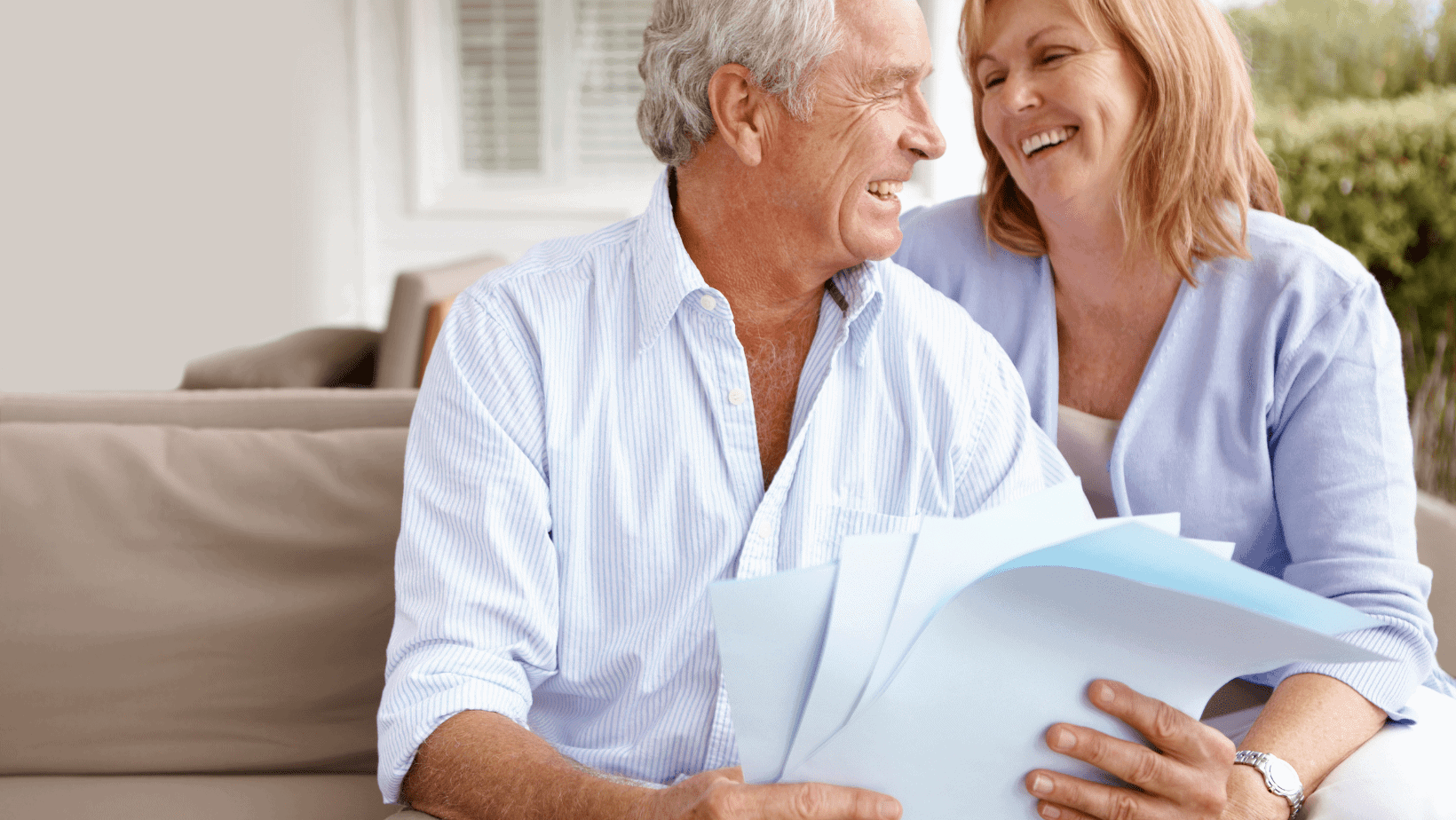 A senior man and a woman smiling and looking at each other while holding papers.