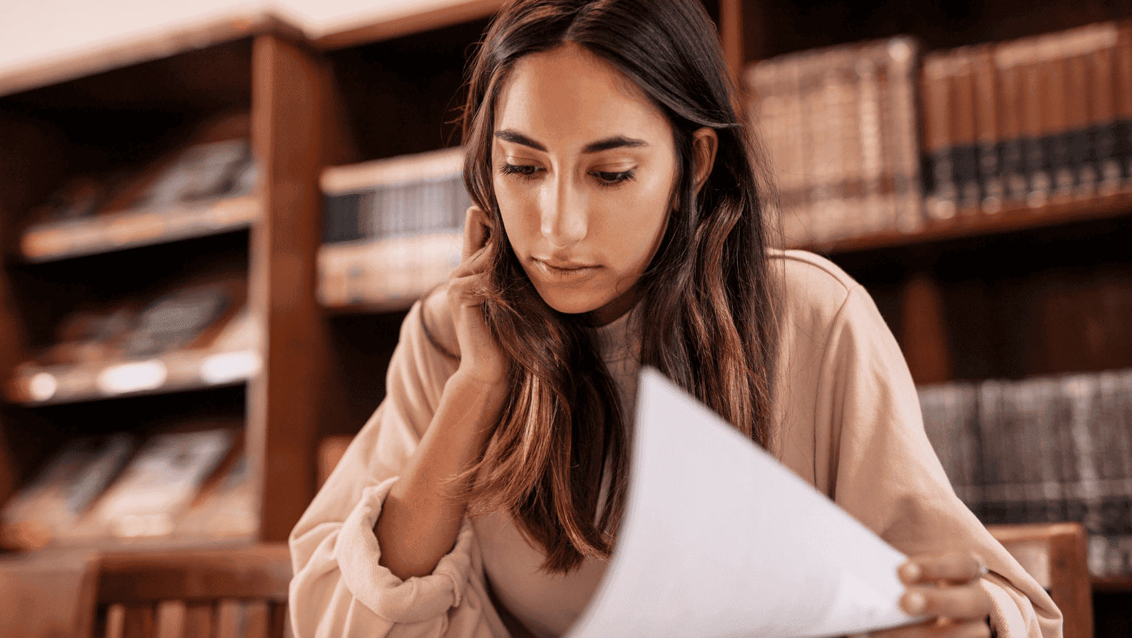 Woman reading a book in a library with wooden shelves.