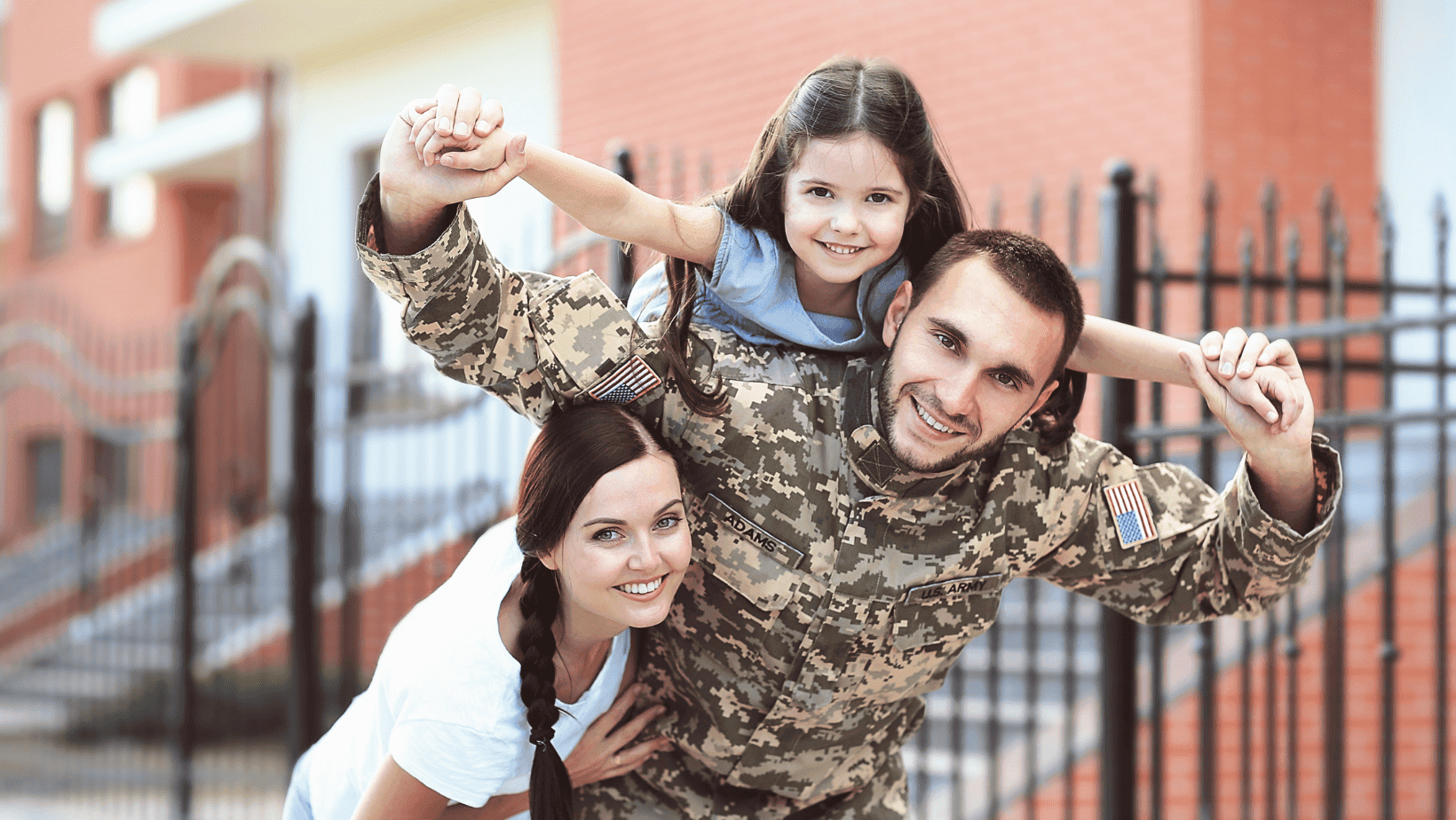 Smiling family with soldier father and young daughter playing outside.
