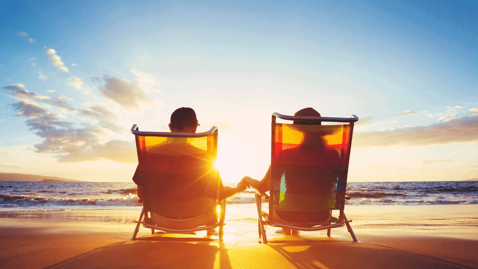 Two people sitting in beach chairs on the beach at sunset.