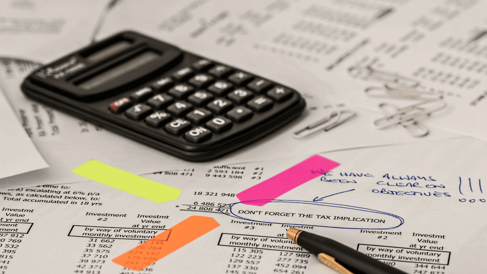 Calculator on financial documents with colorful sticky notes and papers.