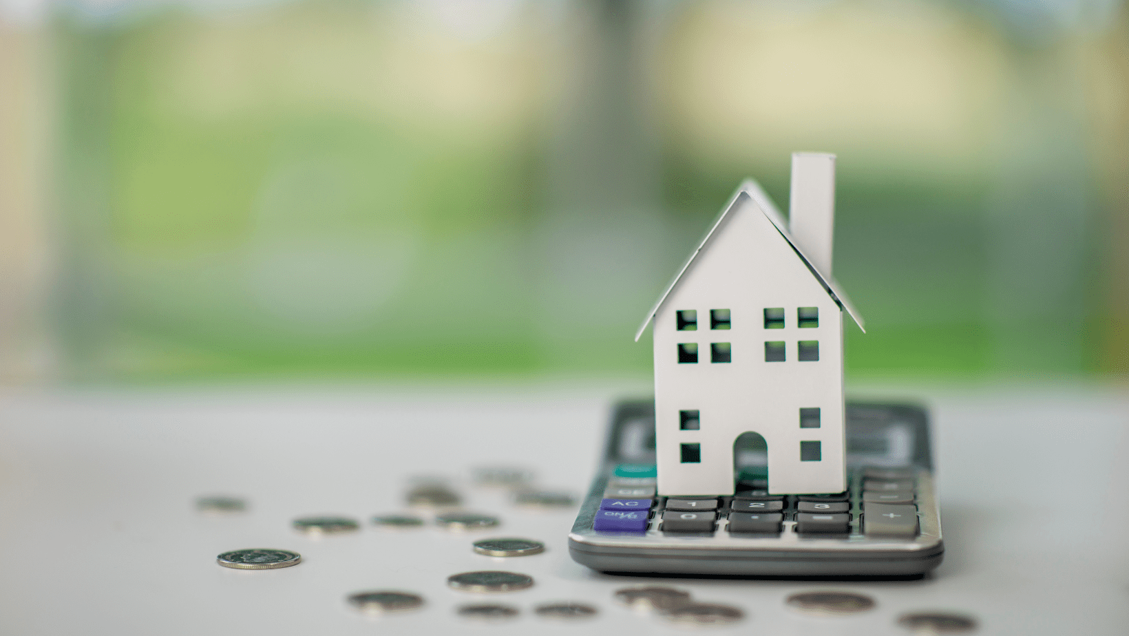 House model on calculator with coins, representing real estate or mortgage calculations.