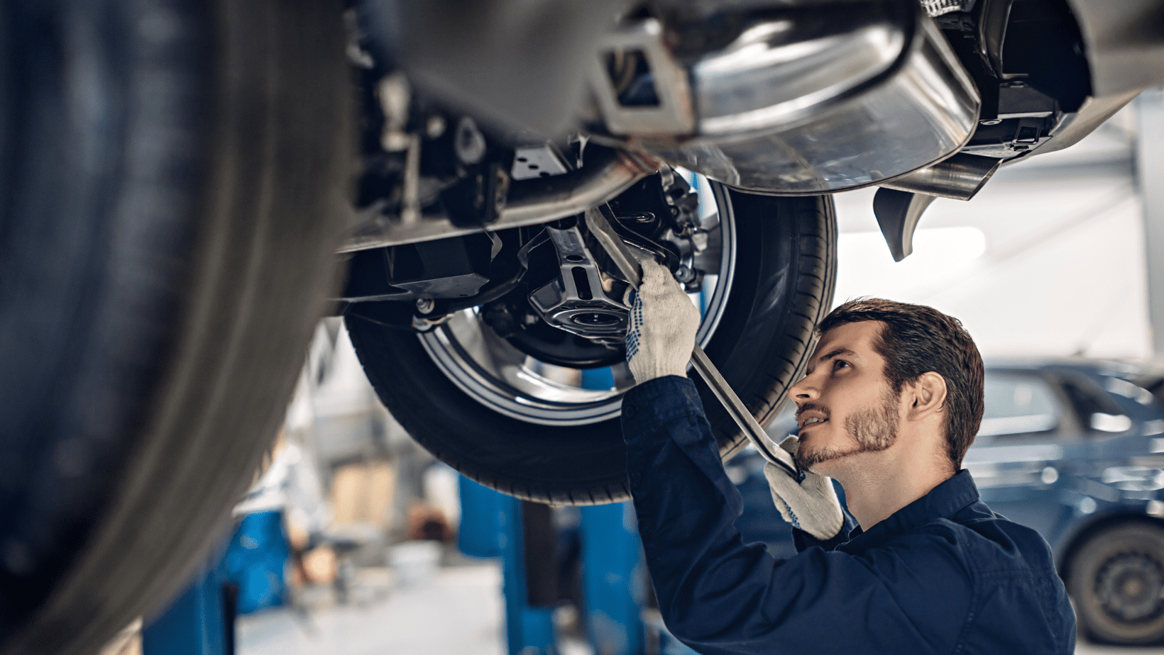 Auto mechanic inspecting car undercarriage with tools in garage.