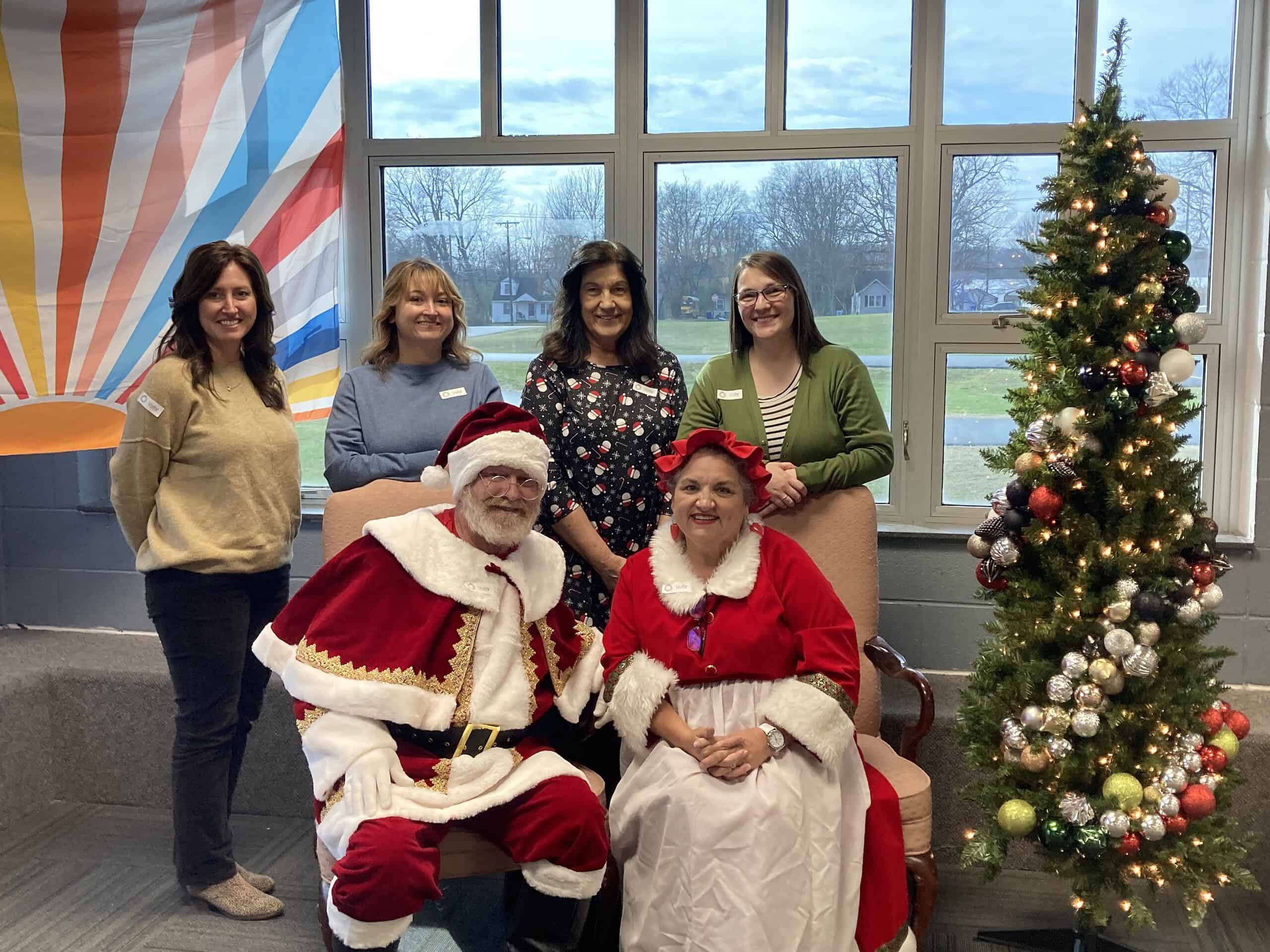 Christmas celebration with Santa and Mrs. Claus with four women in a decorated room. Festive holiday gathering featuring Santa Claus, Mrs. Claus, and four women in a decorated room.