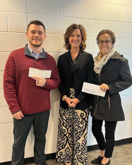 Three people smiling and holding checks in a hallway.