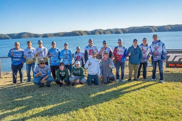 Group of people in racing gear by a lake with hills in the background.