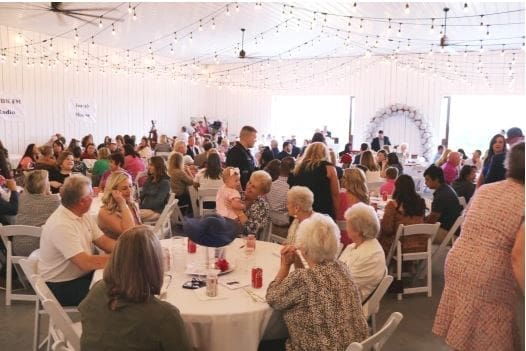 Guests enjoying a celebration event in a decorated venue with string lights and floral arch.