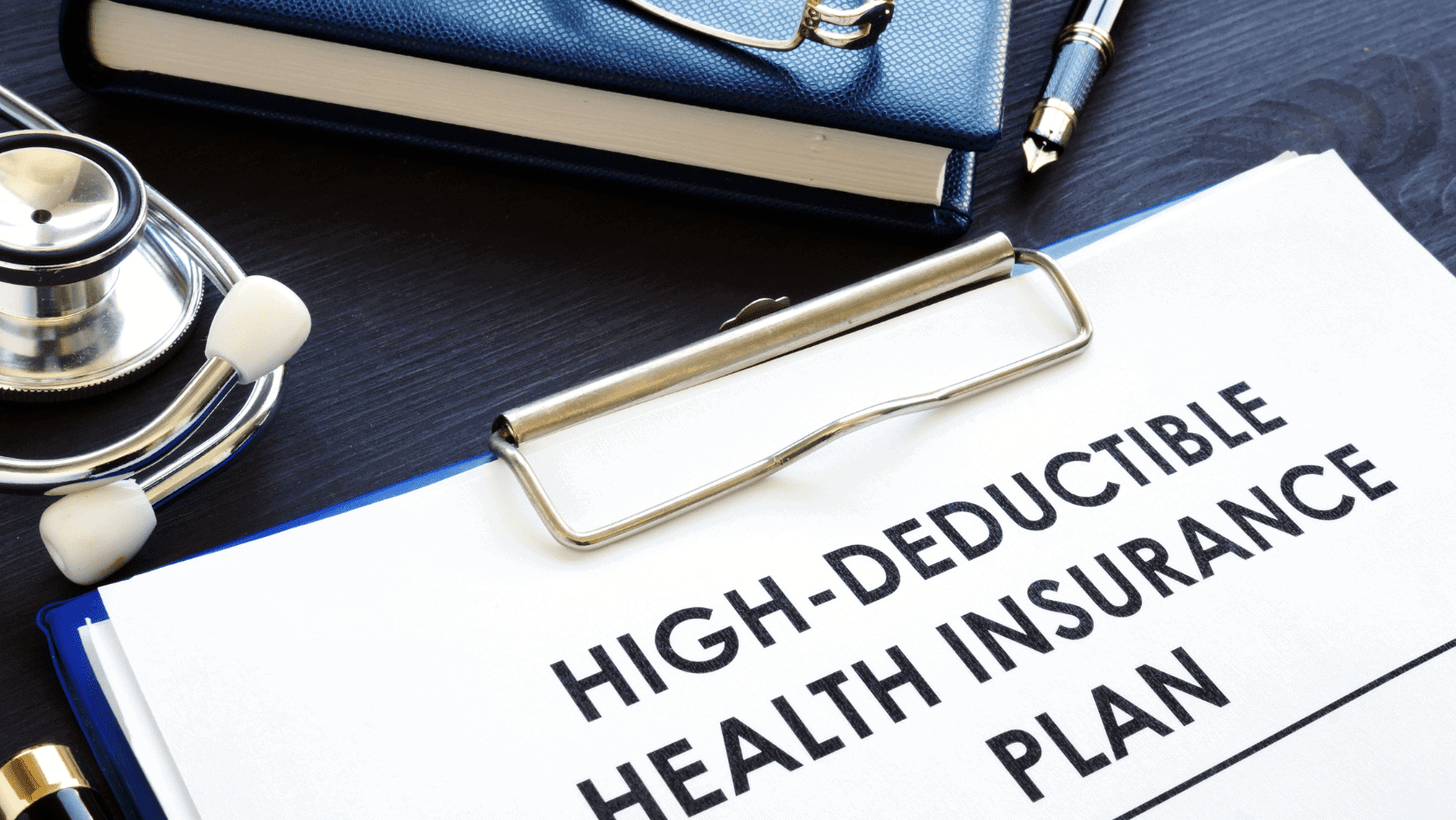 High deductible health insurance plan with a stethoscope, notebook, and pen on a desk.